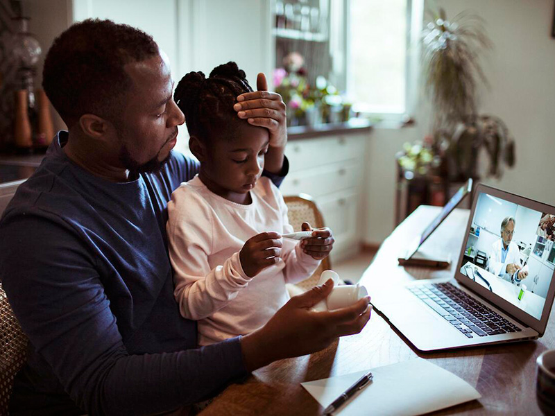 Father holding daughter on Zoom with doctor