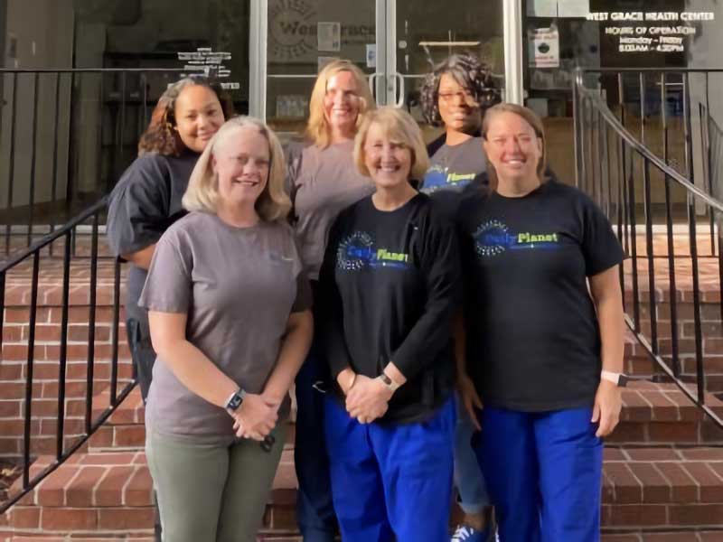 six people with daily planet tee shirts posing and smiling outside the west grace health center