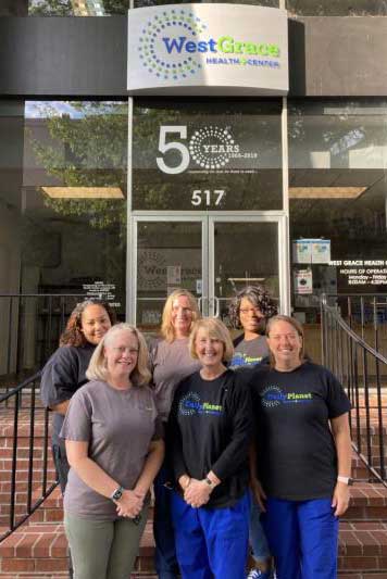 six people with daily planet tee shirts posing and smiling outside the west grace health center