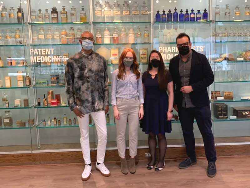 Four members of the Pharmacists for Digital Health student group stand in front of a display of historical pharmacy bottles and tools