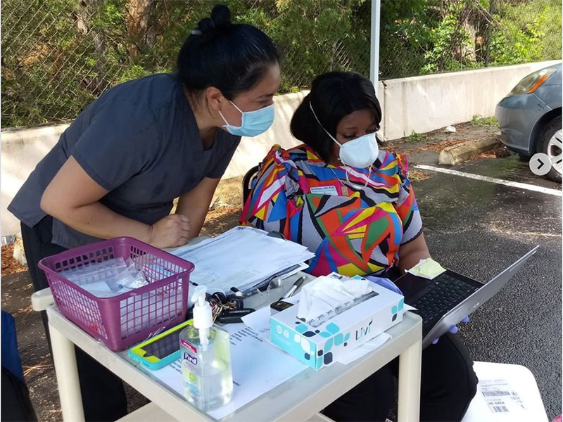 Two health care workers from CrossOver Healthcare Ministry under a tent in a parking lot, running a COVID-19 testing clinic