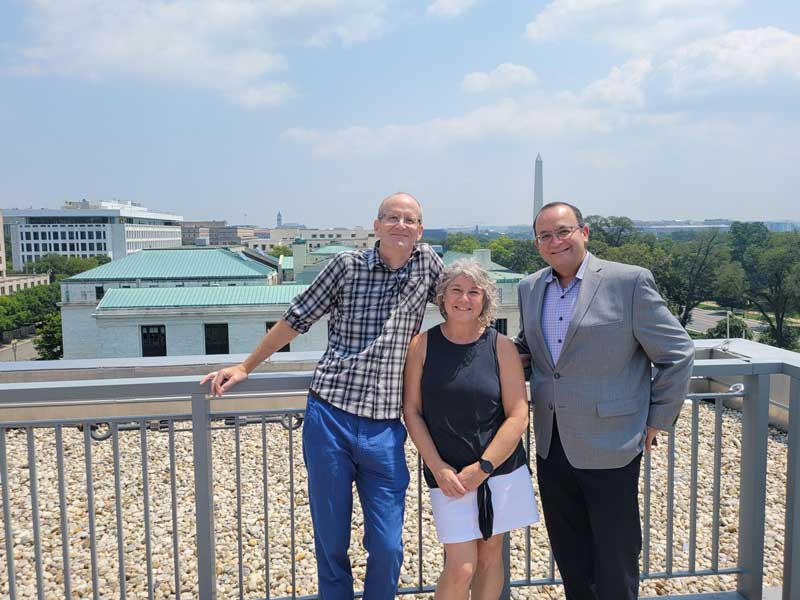 David and Diane Holdford stand side by side smiling with Dr. Rafael Saenz on a balcony in Washington, D.C., at the APhA Headquarters