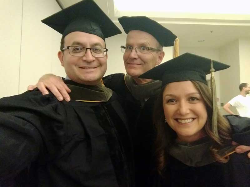 Two smiling Pharm.D. grads, Rafael Saenz and Leigh Anne Hylton Gravatt, take a selfie with a grinning Dr. Holdford at their graduation ceremony in 2003.